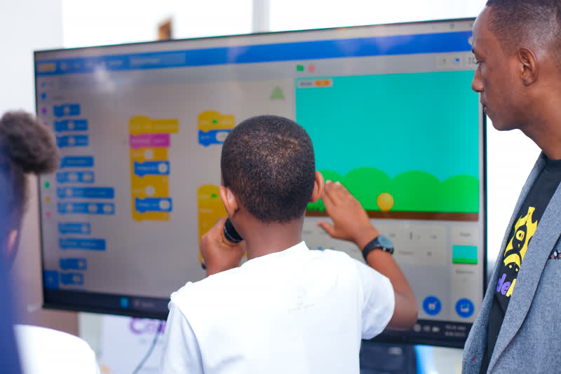 A child dragging Scratch blocks on a big touchscreen while a mentor watches