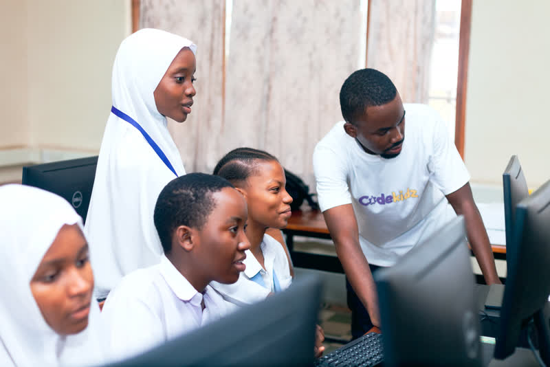 Students working at computers with a CodeKidz mentor beside them